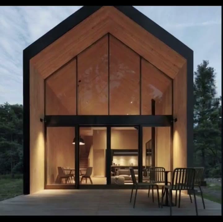 A glass-gabled cabin glowing warm against the pines at dusk
